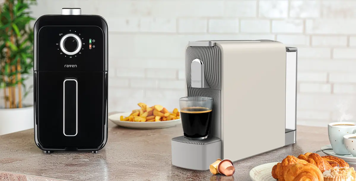 Чорна аерофритюрниця Raven та сіро-бежева кавоварка із завареною кавою у склянці на кухонній стільниці, на задньому плані кава та закуски.