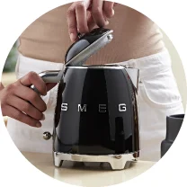 Людина тримає чорний чайник Smeg з відкритою кришкою