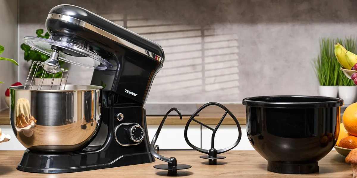 Планетарний міксер Zelmer з металевою чашею, пластиковою чашею поруч і двома насадками для змішування на кухонній стільниці.