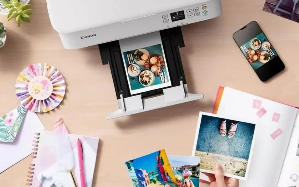 Принтер Canon PIXMA друкує фотографії, вид зверху, поруч смартфон і фотоальбом