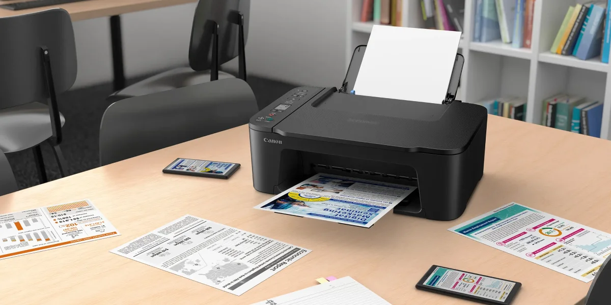 Canon PIXMA TS3750i на офісному столі друкує документи, навколо розкладені аркуші паперу та смартфони