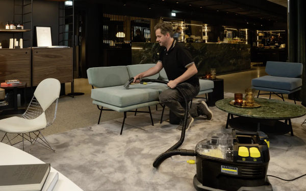 Чоловік пилососить диван пилососом Karcher Puzzi 8/1 Anniversary Edition в елегантній вітальні.