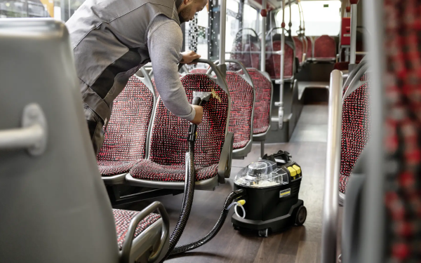 Чоловік використовує пилосос Karcher Puzzi 8/1 Anniversary Edition для чищення сидінь автобуса.