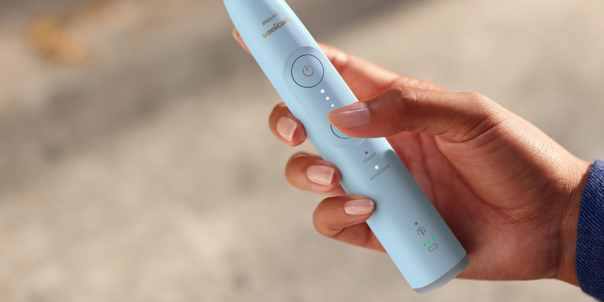 Людина тримає в руці синю зубну щітку Philips Sonicare Sonicare HX7406/02 на розмитому фоні.