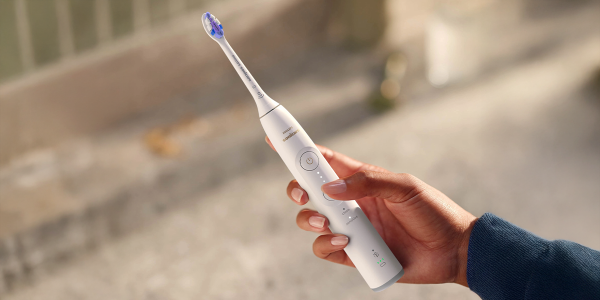 Людина тримає в руці білу зубну щітку Philips Sonicare Sonicare HX7400/01 на розмитому фоні.