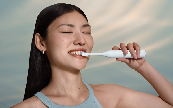 Усміхнена жінка чистить зуби білою зубною щіткою Philips Sonicare HX7400/01.