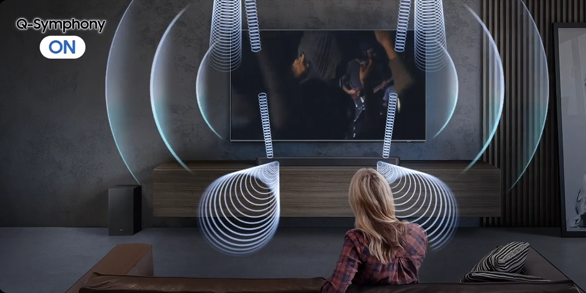 Жінка сидить на дивані перед телевізором, уявляючи собі об'ємний звук із саундбара та динаміків телевізора.