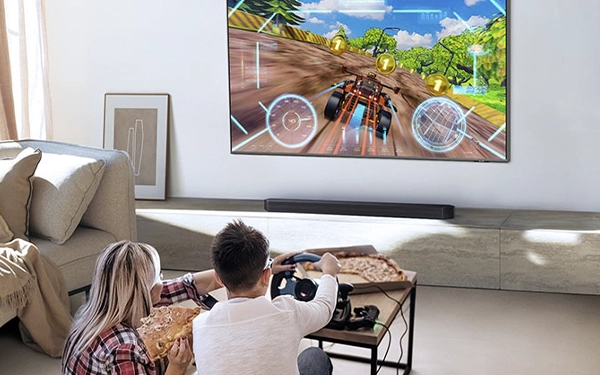 Діти грають у гонки перед телевізором, а під екраном розміщено саундбар