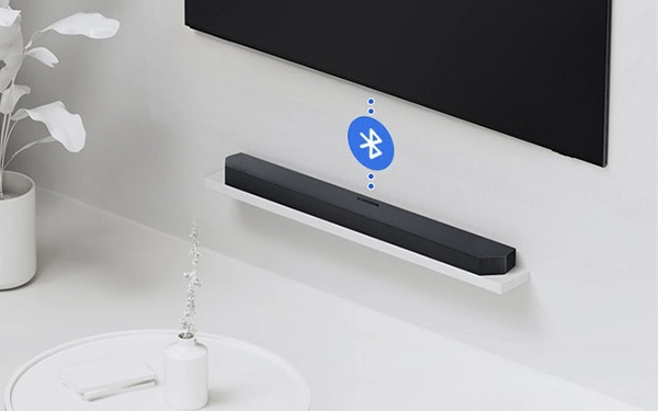 Саундбар, встановлений під телевізором на стіні, з іконкою Bluetooth, що символізує бездротове з’єднання.