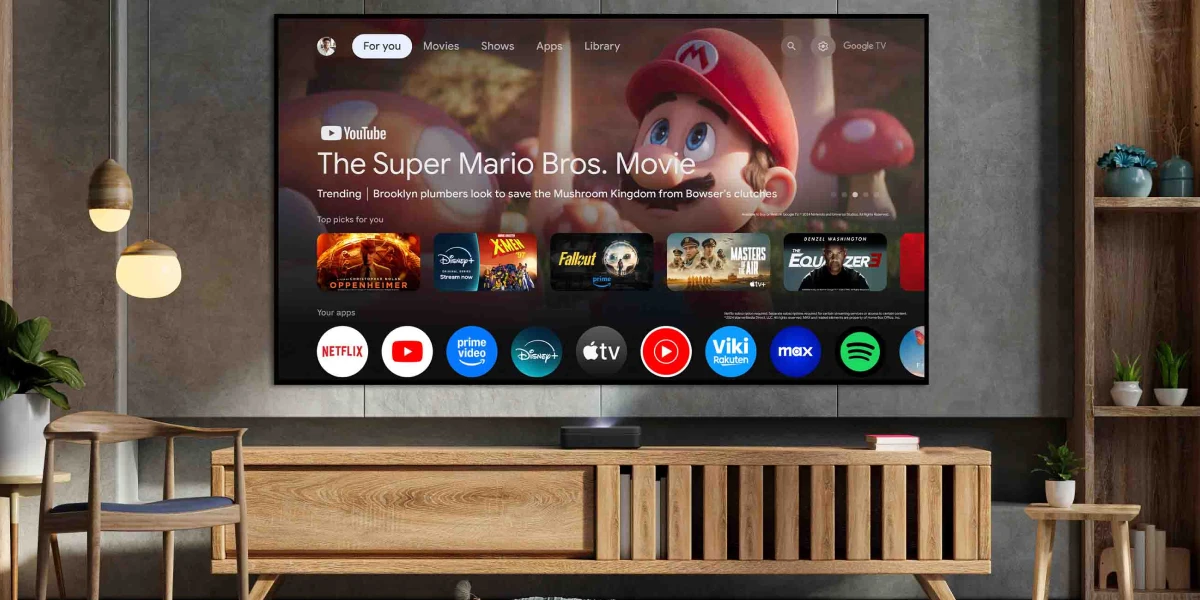 Лазерний проектор Optoma Photon Go Laser, розміщений у вітальні під телевізором, з додатками Google TV на екрані