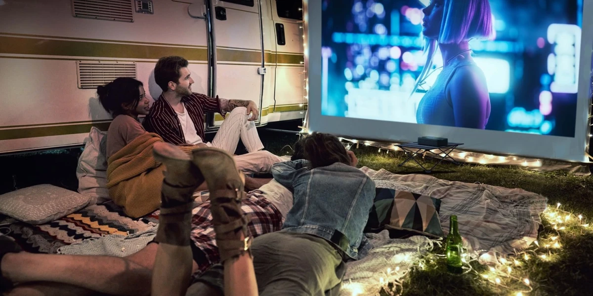 Фільм проектується з лазерного проектора Optoma Photon Go на екран біля кемперу, а люди сидять на ковдрах та подушках.