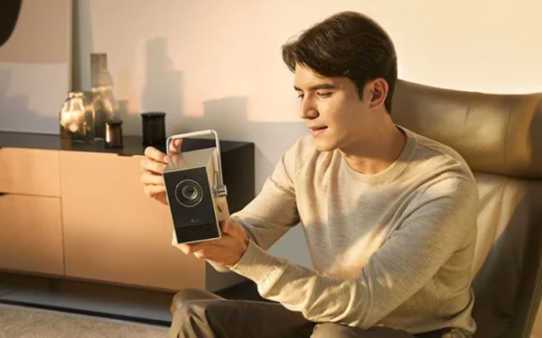 Чоловік тримає проектор LG CineBeam Q, сидячи у своїй вітальні.