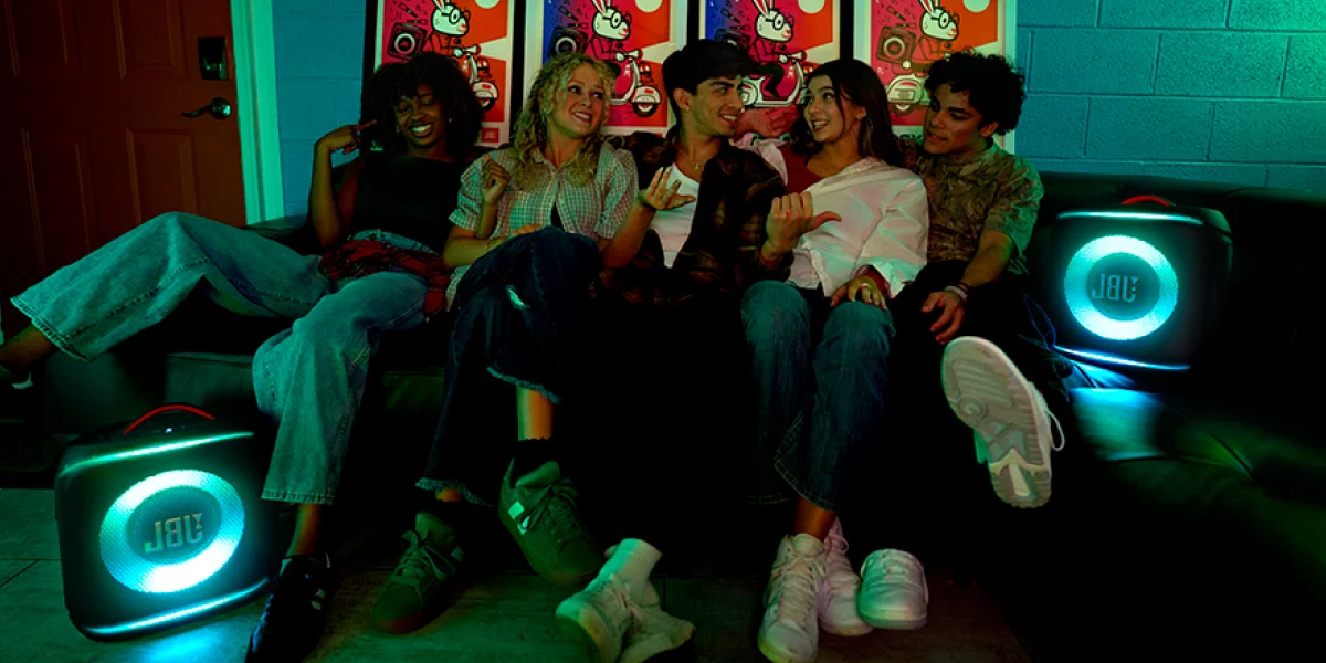 П'ятеро людей сидять на дивані, поруч із ними дві яскраві колонки JBL створюють атмосферу вечірки