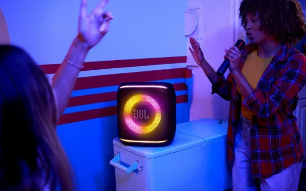 Людина співає в мікрофон поруч із динаміком JBL з рожево-жовтим підсвічуванням.