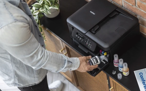 Чоловік заправляє чорнильний контейнер принтера Brother DCP-T735DW, стоячи на шафі.