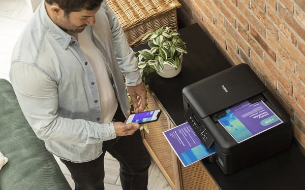 Чоловік друкує зі свого мобільного телефону на принтері Brother DCP-T735DW, який лежить на шафі.