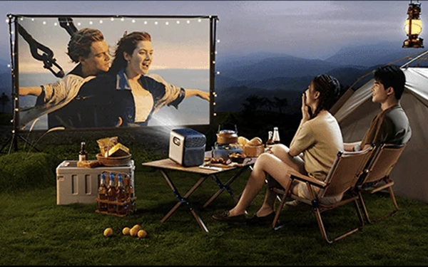 Двоє людей дивляться фільм, що проектується на екран, під час вечірнього походу з наметами в горах.