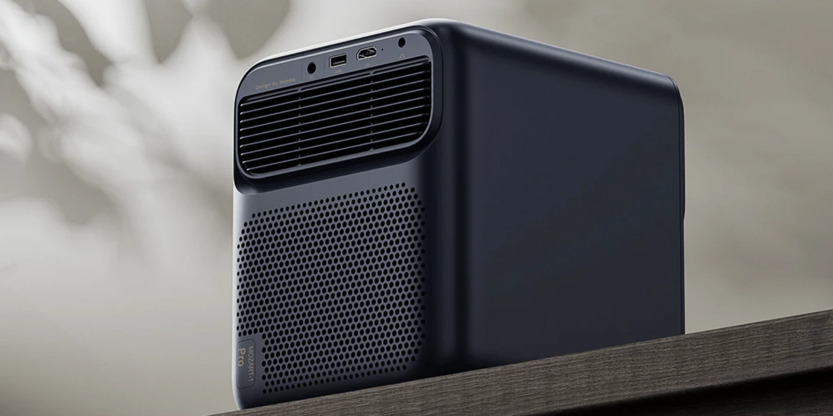 Задня частина проектора Wanbo з вентиляційним отвором та портами, розміщеного на дерев'яній полиці на тлі розмитої стіни.