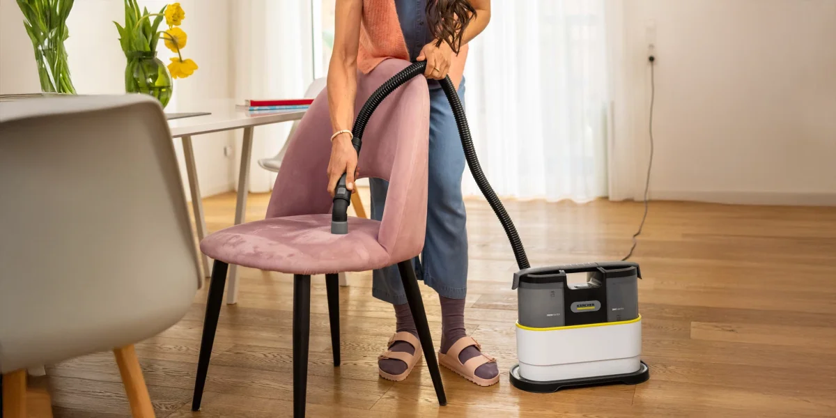 Людина чистить рожеве крісло пилососом Karcher SE 2 Spot у світлій вітальні.