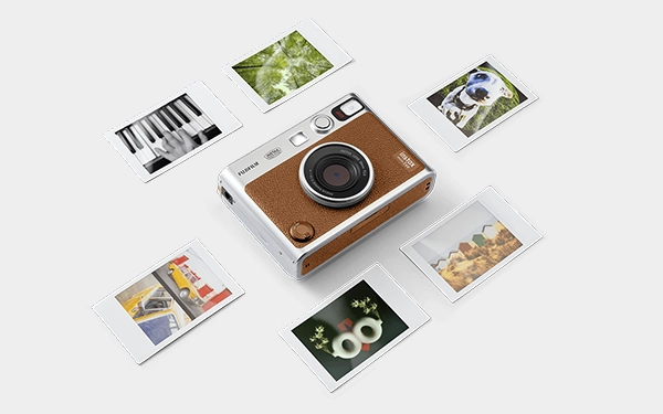 Коричнева камера Instax Mini Evo лежить пласко на білому тлі. По всьому пристрою розкидані барвисті фотографії.