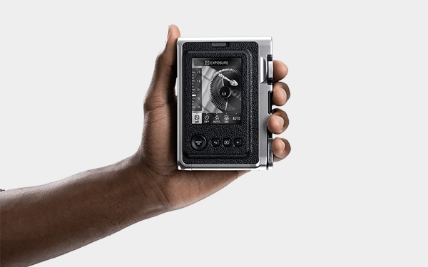 Рука тримає срібну камеру, дивлячись на задній екран. На дисплеї відображається цифровий інтерфейс із графікою з ефектом об'єктива.