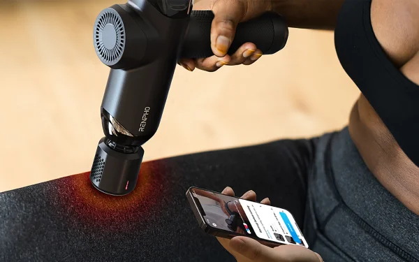 Жінка використовує масажер Renpho Power ThermaCool на стегні, тримаючи телефон в іншій руці.