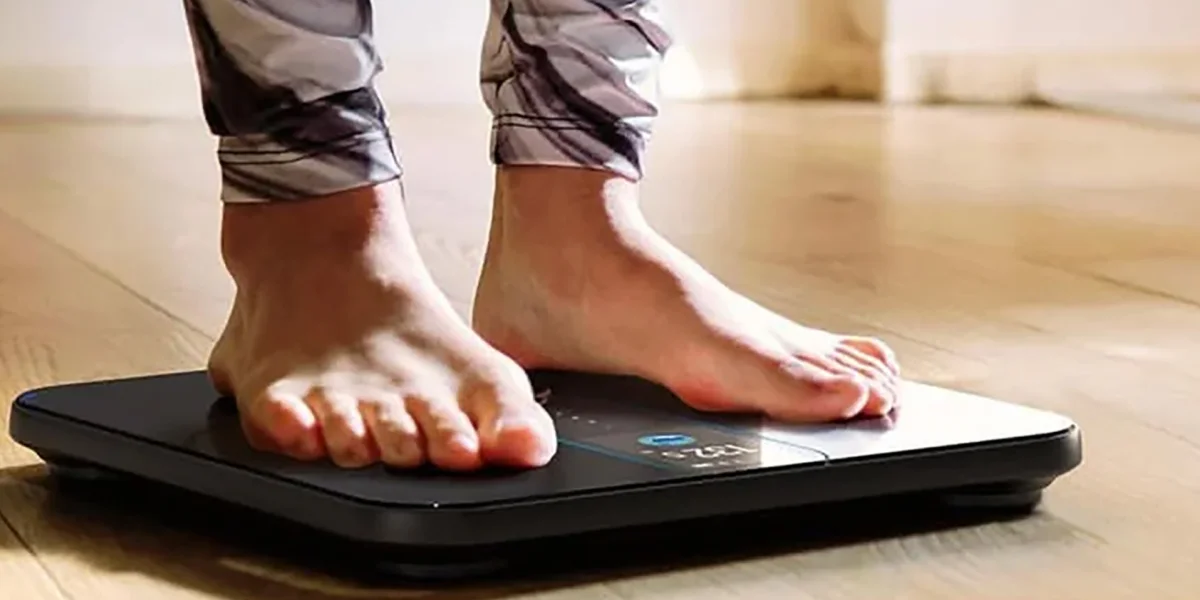 Людина стоїть босоніж на чорній шкалі Renpho Elis Nova на дерев'яній підлозі