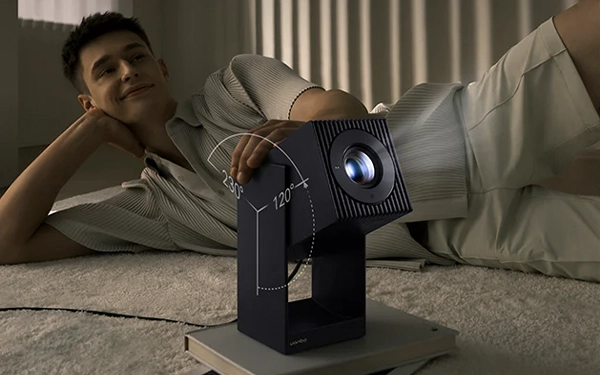 Чоловік лежить на килимі поруч із проектором Wanbo Cube, позначений діапазон обертання корпусу під час регулювання кута проекції.