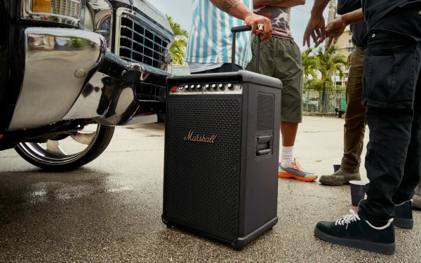 Портативна колонка Marshall з висувною ручкою поруч з автомобілем та кількома людьми