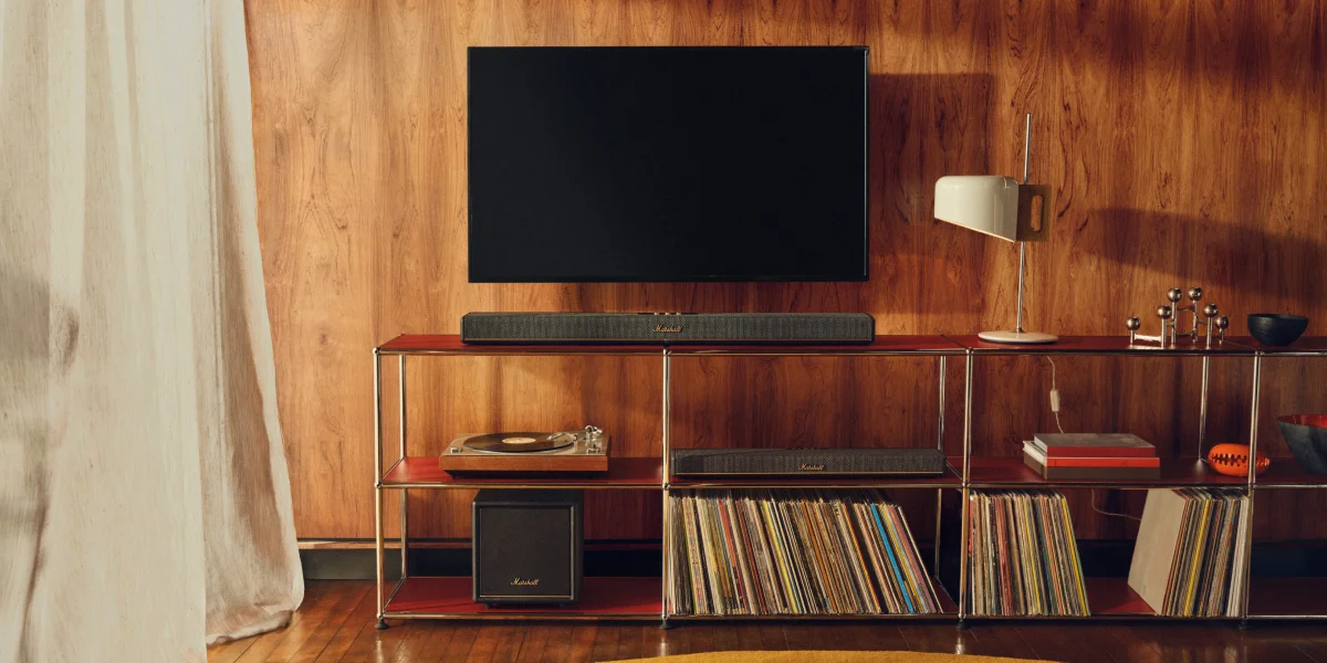 Вітальня з телевізором та саундбаром Marshall на полиці, поруч програвач програвача та вінілові платівки